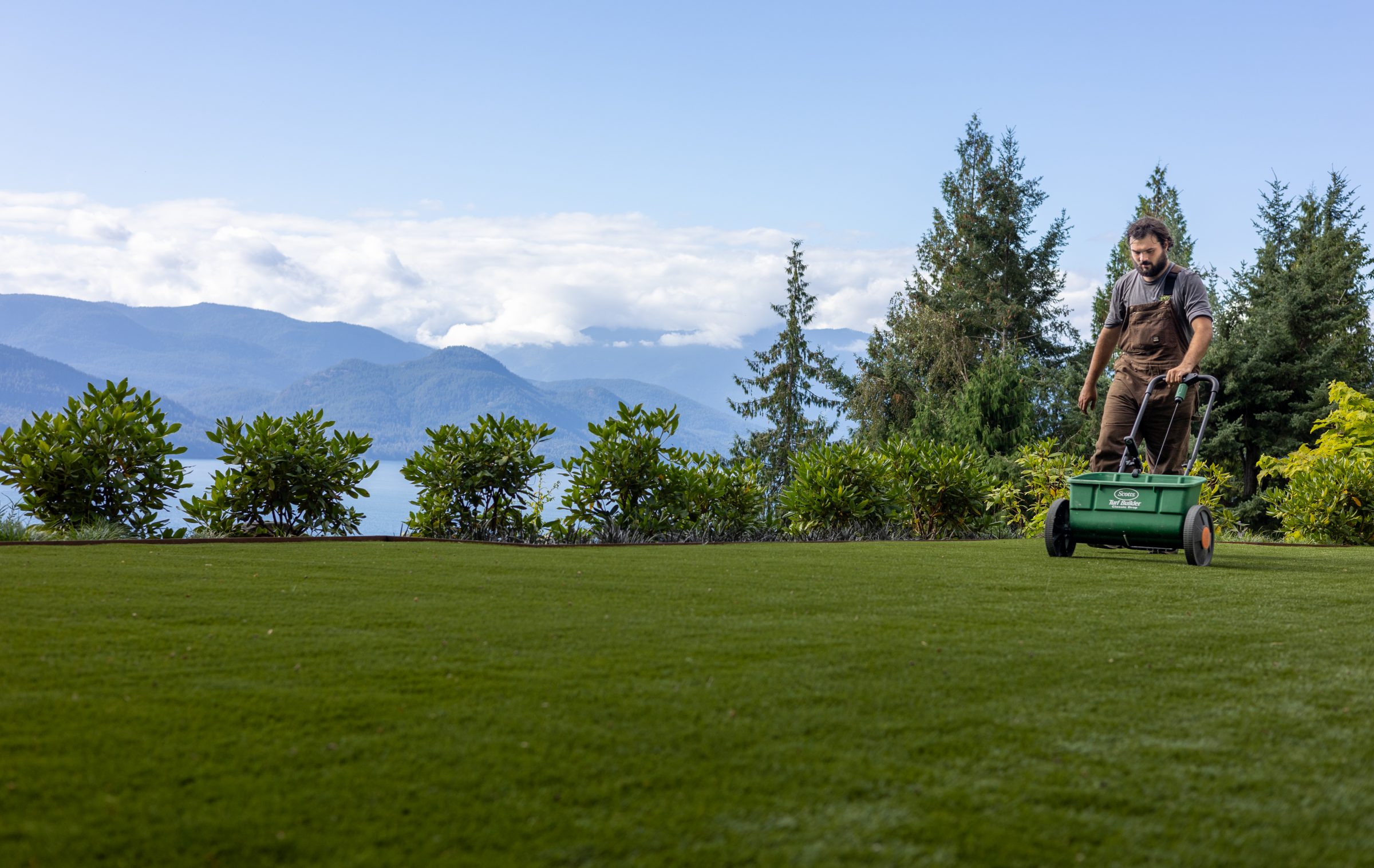 Man distributing fertilizer on lawn with mountain backdrop