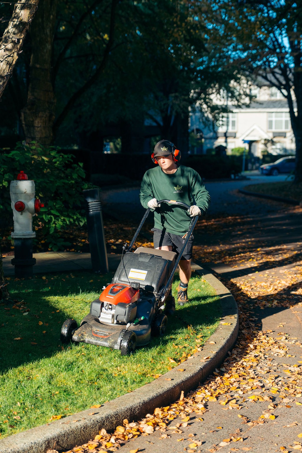 Landscaper mowing grass along residential sidewalk curb