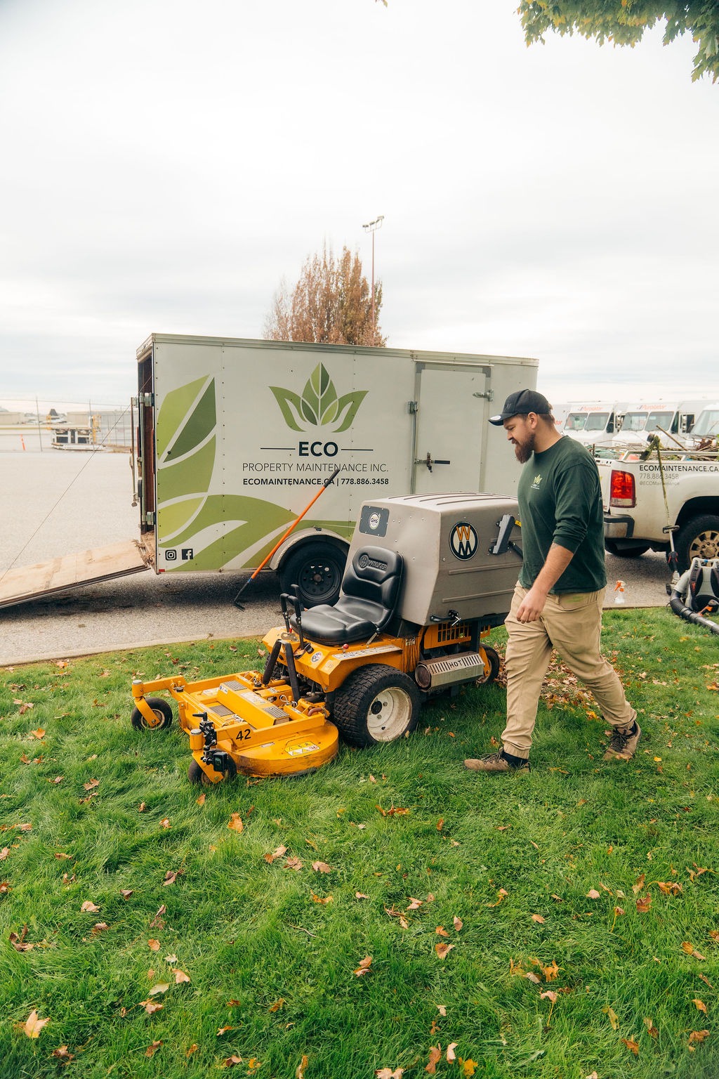 Landscaper with ride-on mower near maintenance trailer