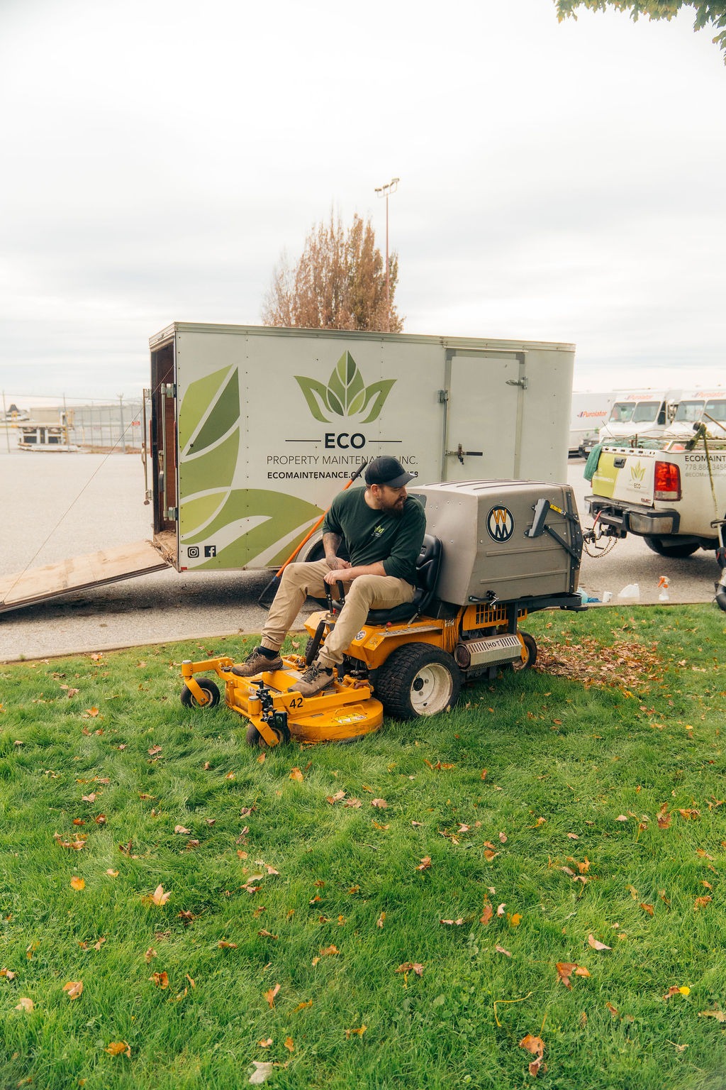 Worker riding lawn mower beside maintenance trailer