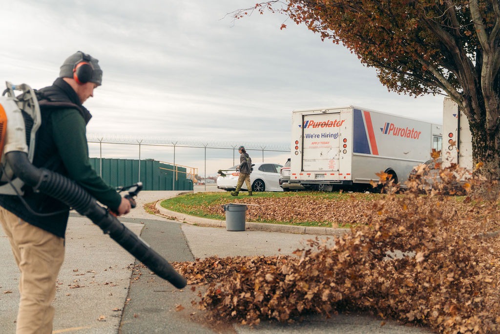 Worker blowing autumn leaves in parking lot