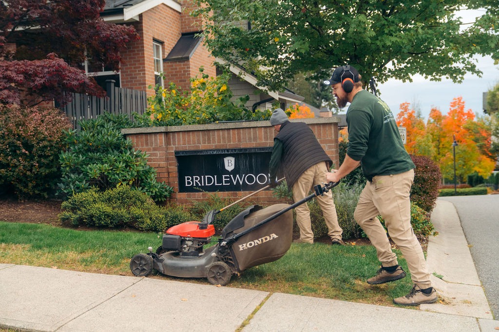 Landscapers mowing lawn near neighbourhood entrance sign