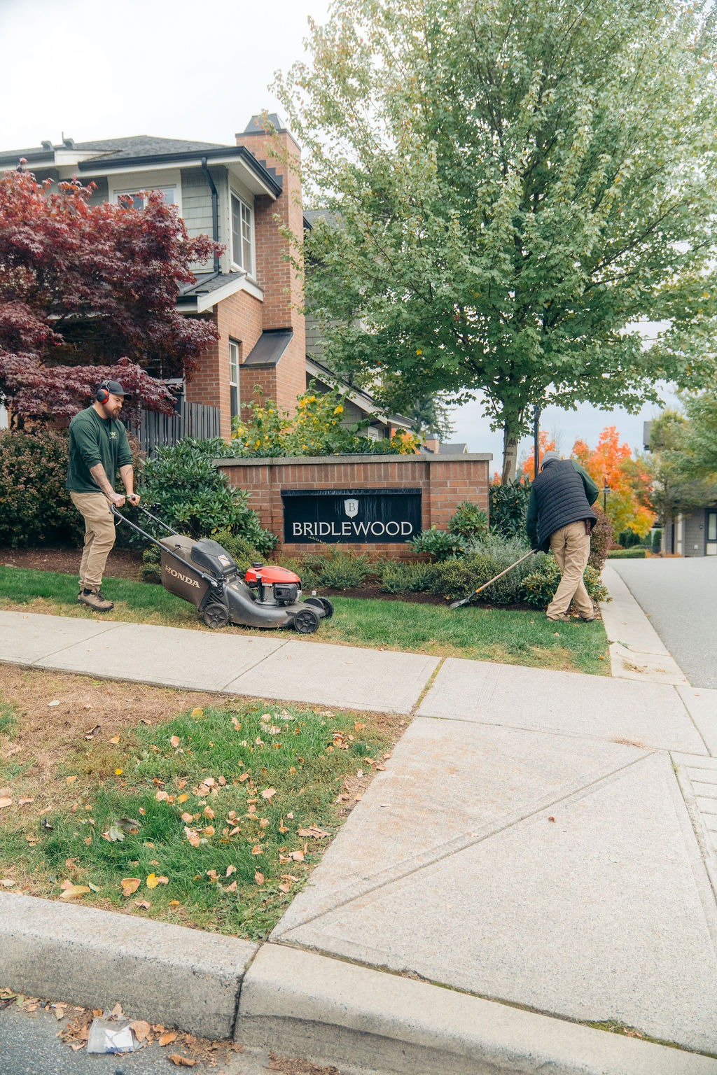 Landscapers mowing lawn near Bridlewood neighbourhood sign