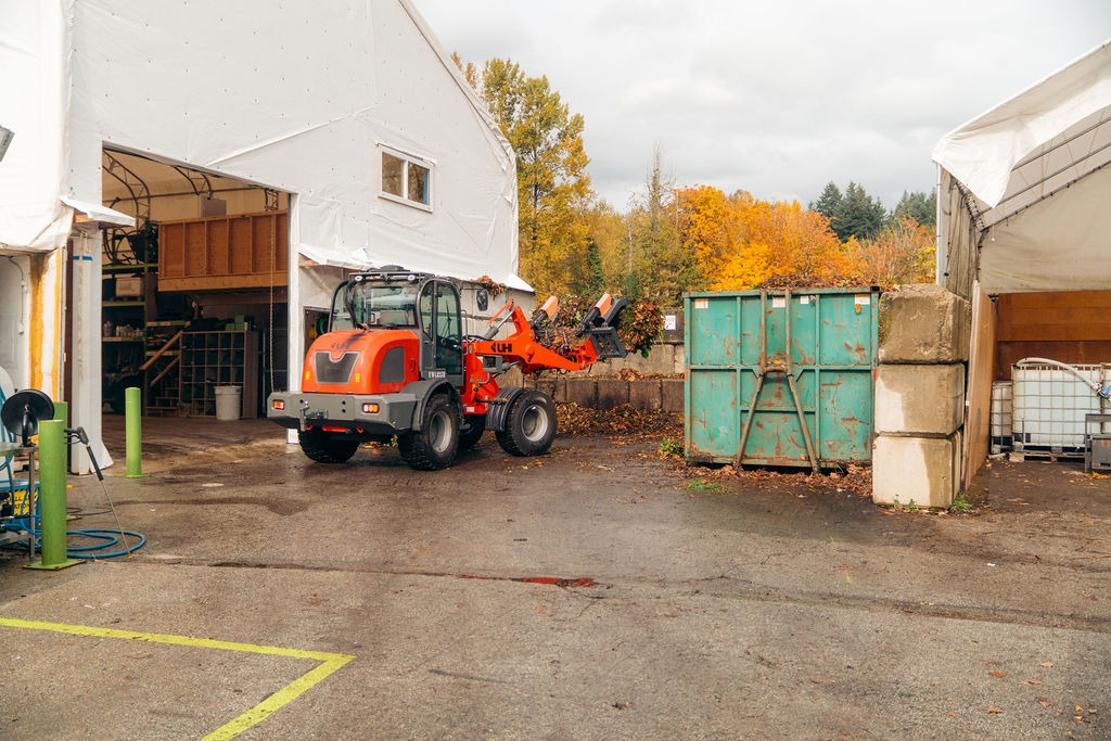 Orange loader beside green dumpster in industrial yard
