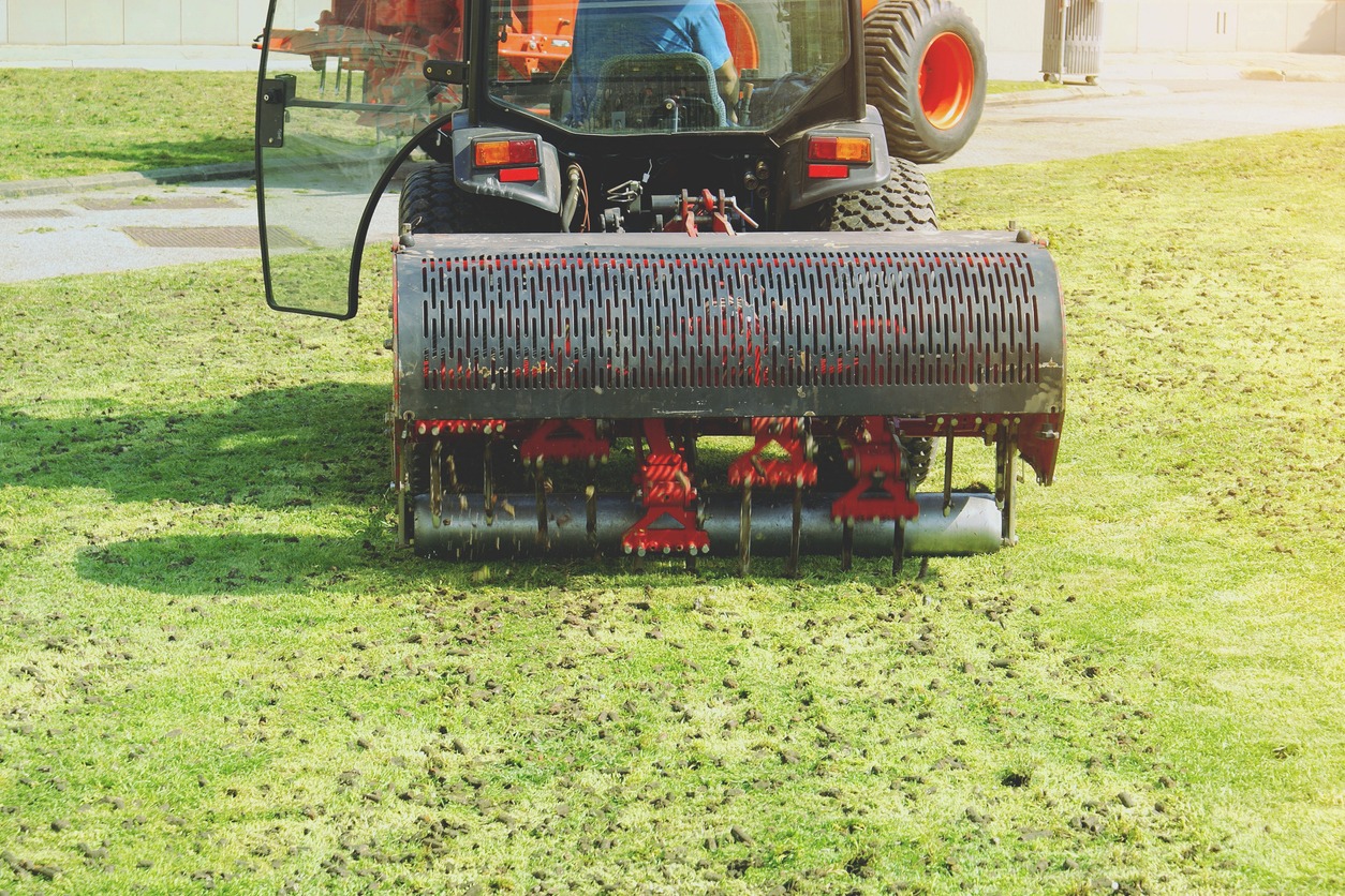 Tractor aerating grass field with heavy machinery