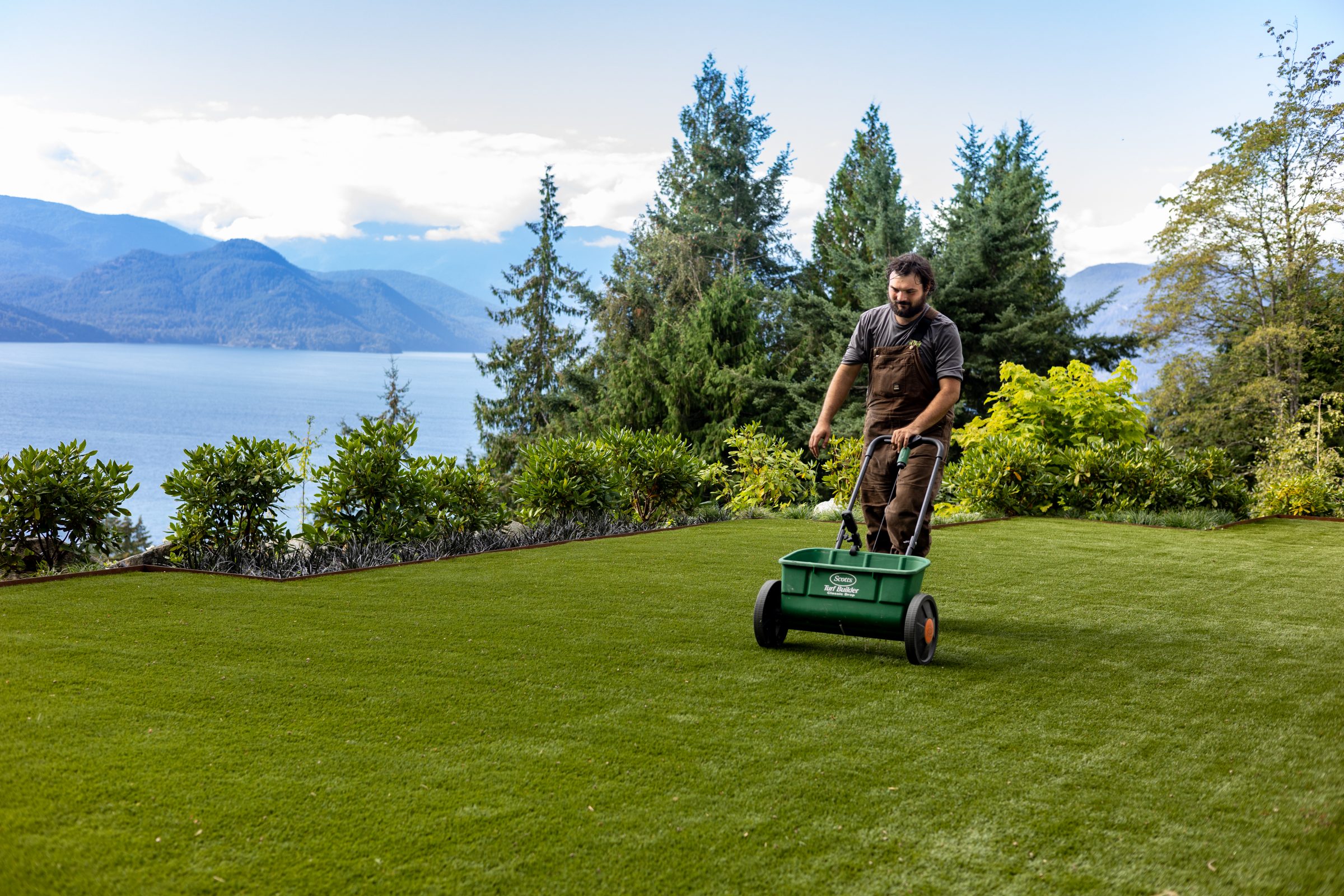 Man distributing fertilizer on lakeside lawn
