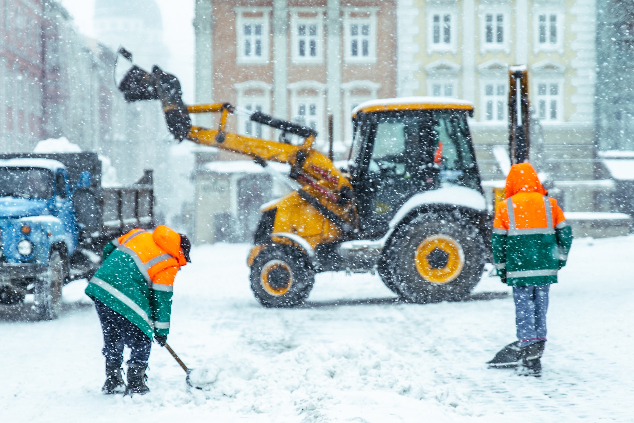 Workers clearing snow with industrial equipment and shovels in snowfall