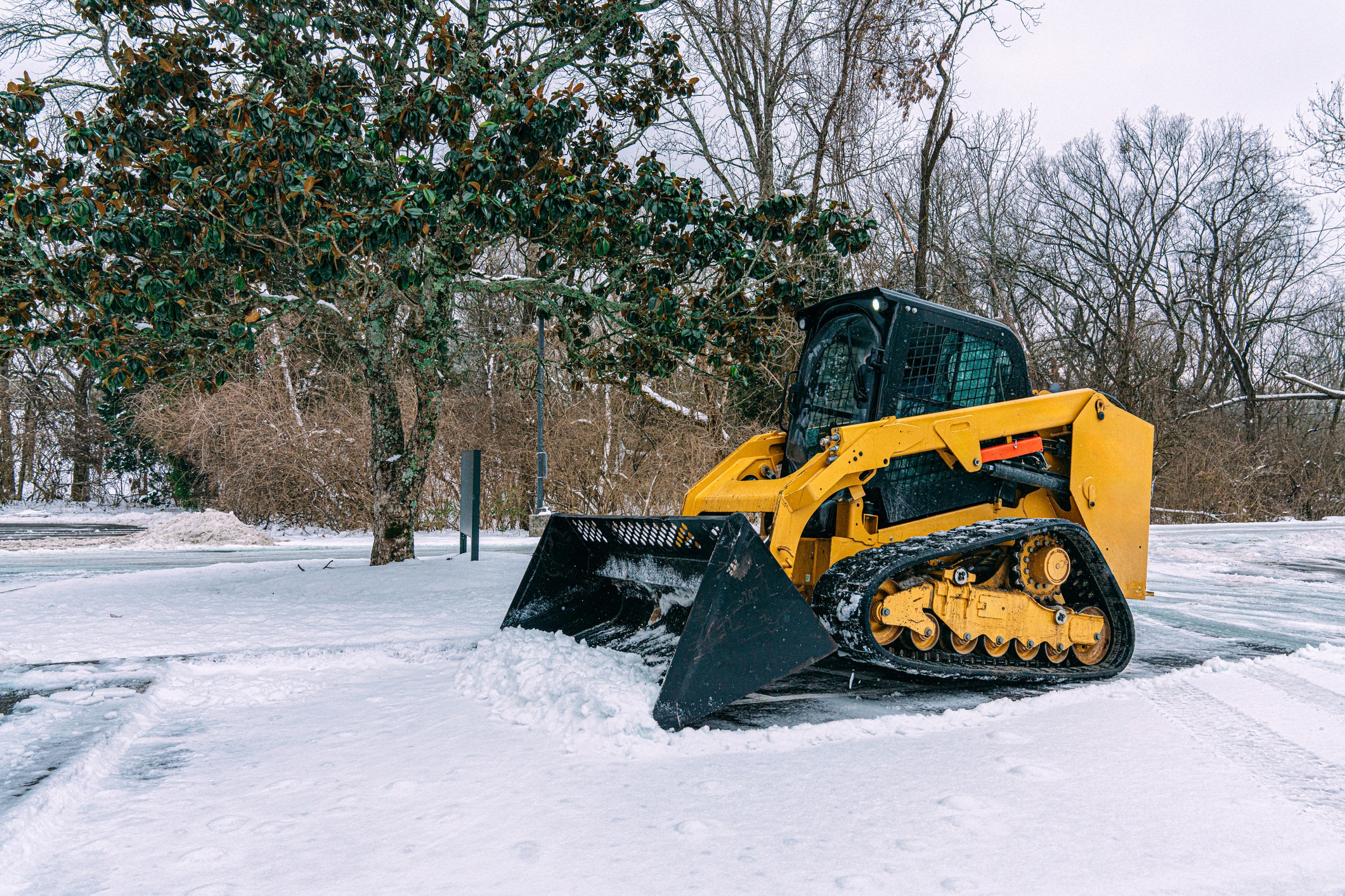 Yellow skid-steer loader clearing snow in winter