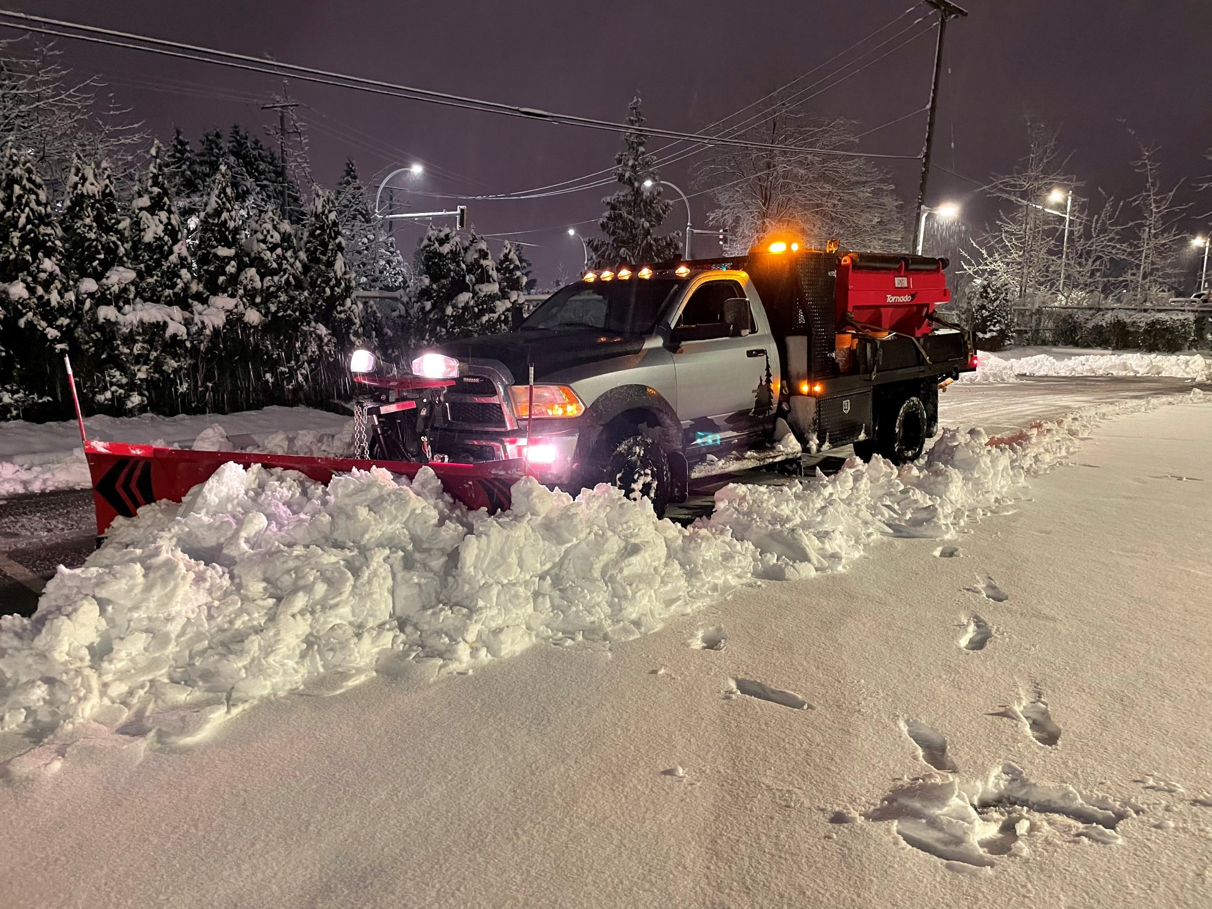 Snowplow truck clearing snow on a street at night