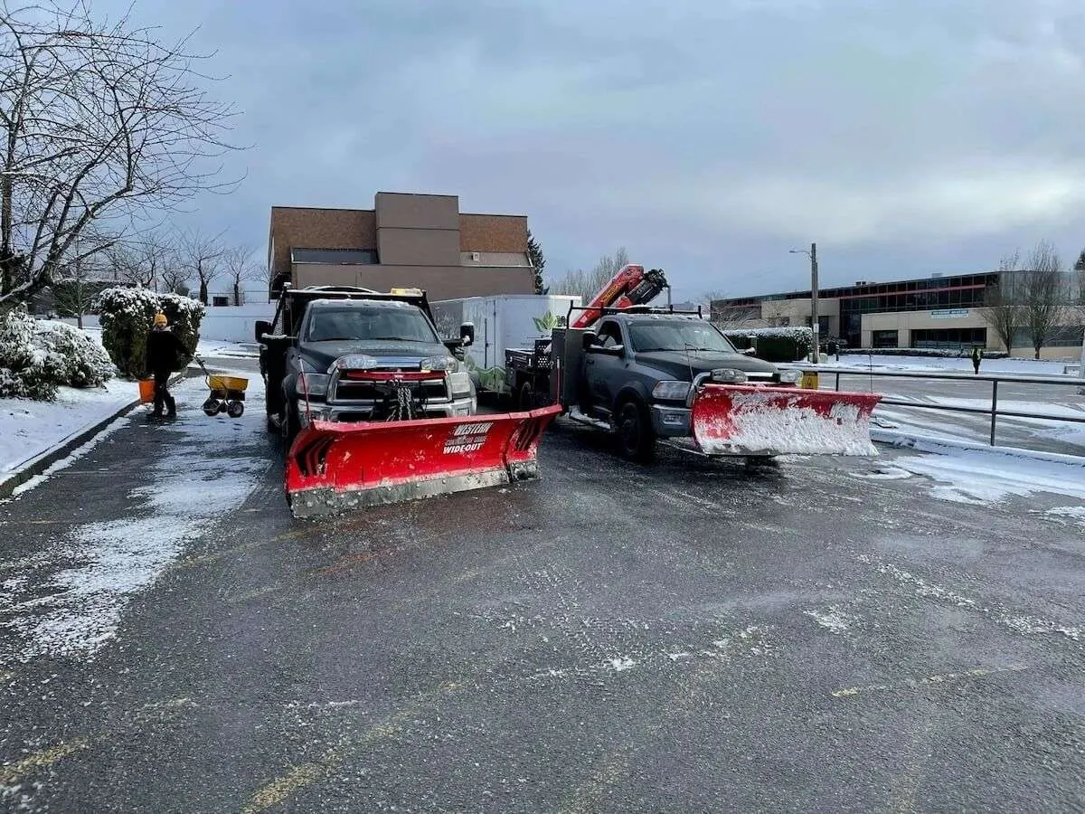 Two trucks with snowplows clearing icy parking lot